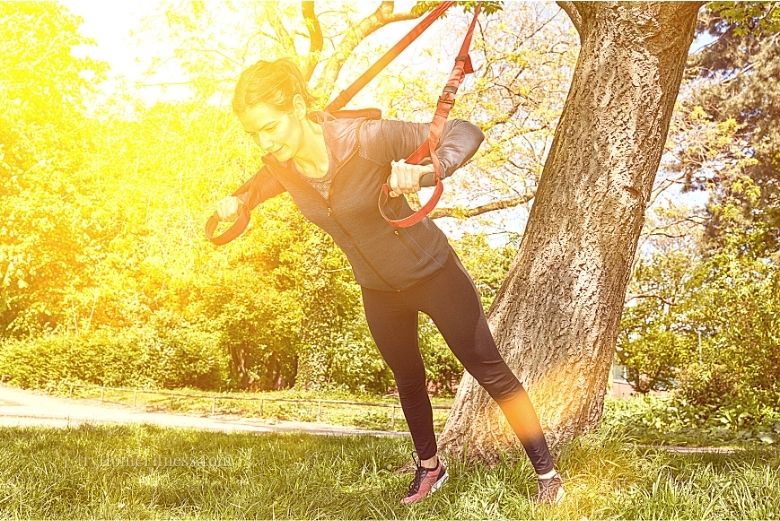 Suspension training benefits one of which shown here where a woman is training outside using a tree