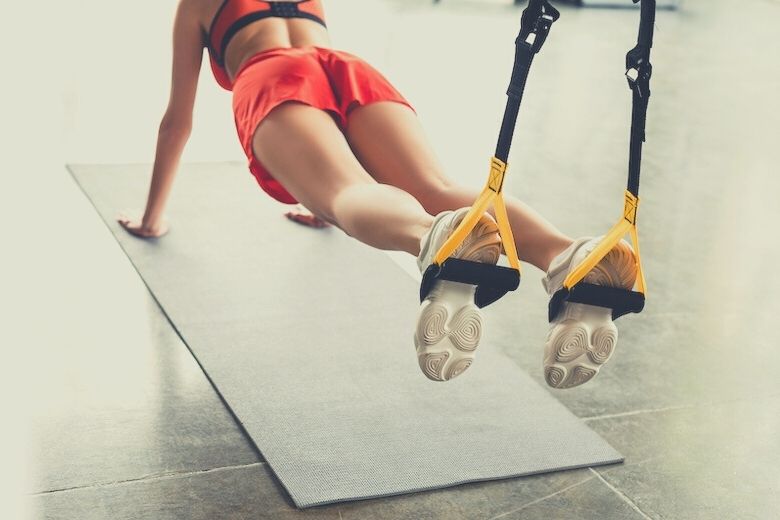 for this suspension training vs resistance bands comparison a cropped woman doing a pushup whilst her feet are suspended in trx trainers